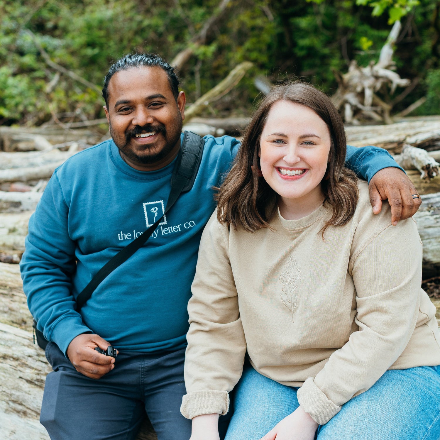 Two people sitting on logs in a forest setting