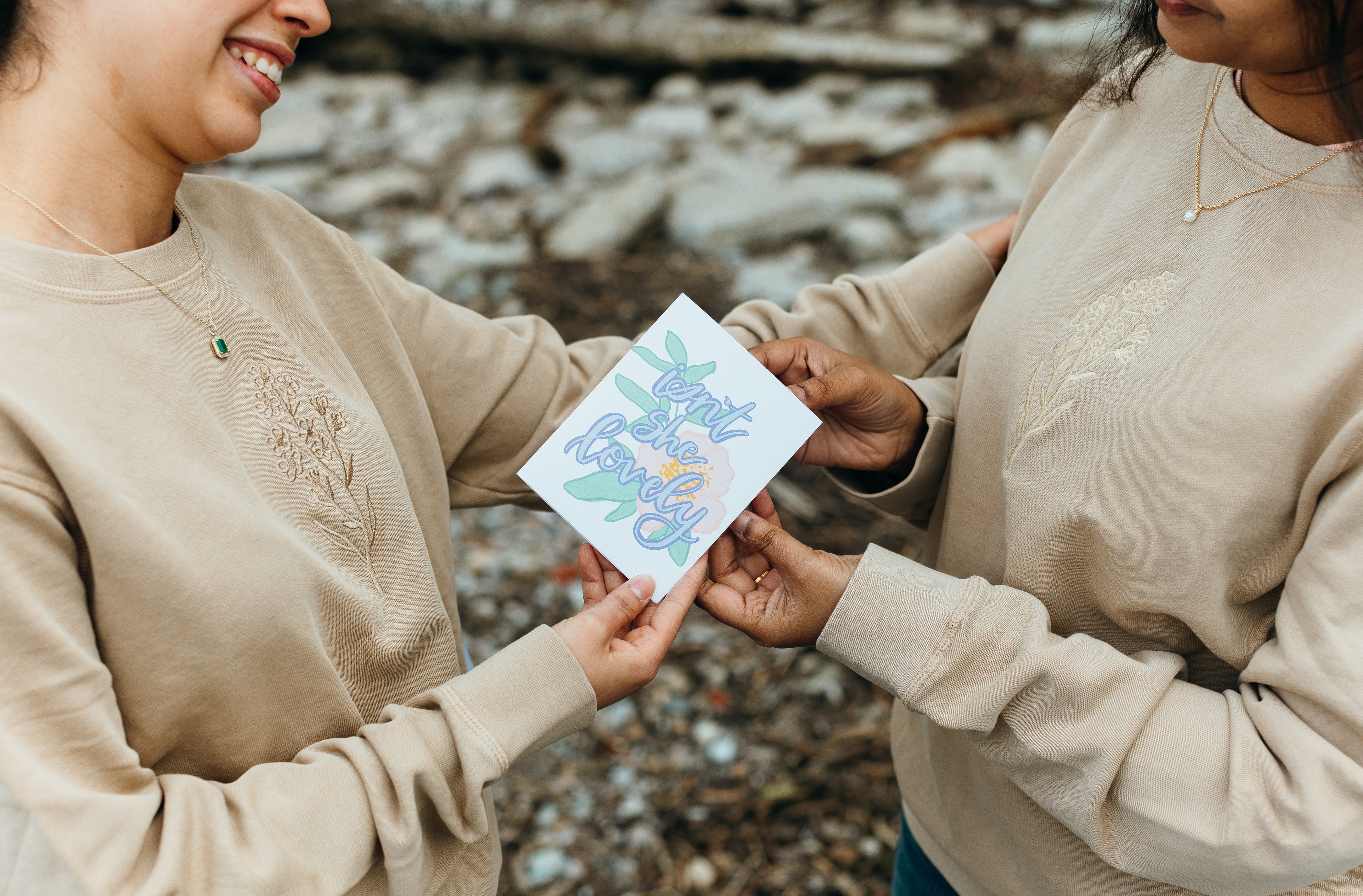 Two people holding a card outdoors with a natural background