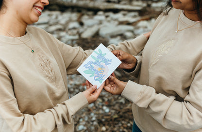 Two people holding a card outdoors with a natural background