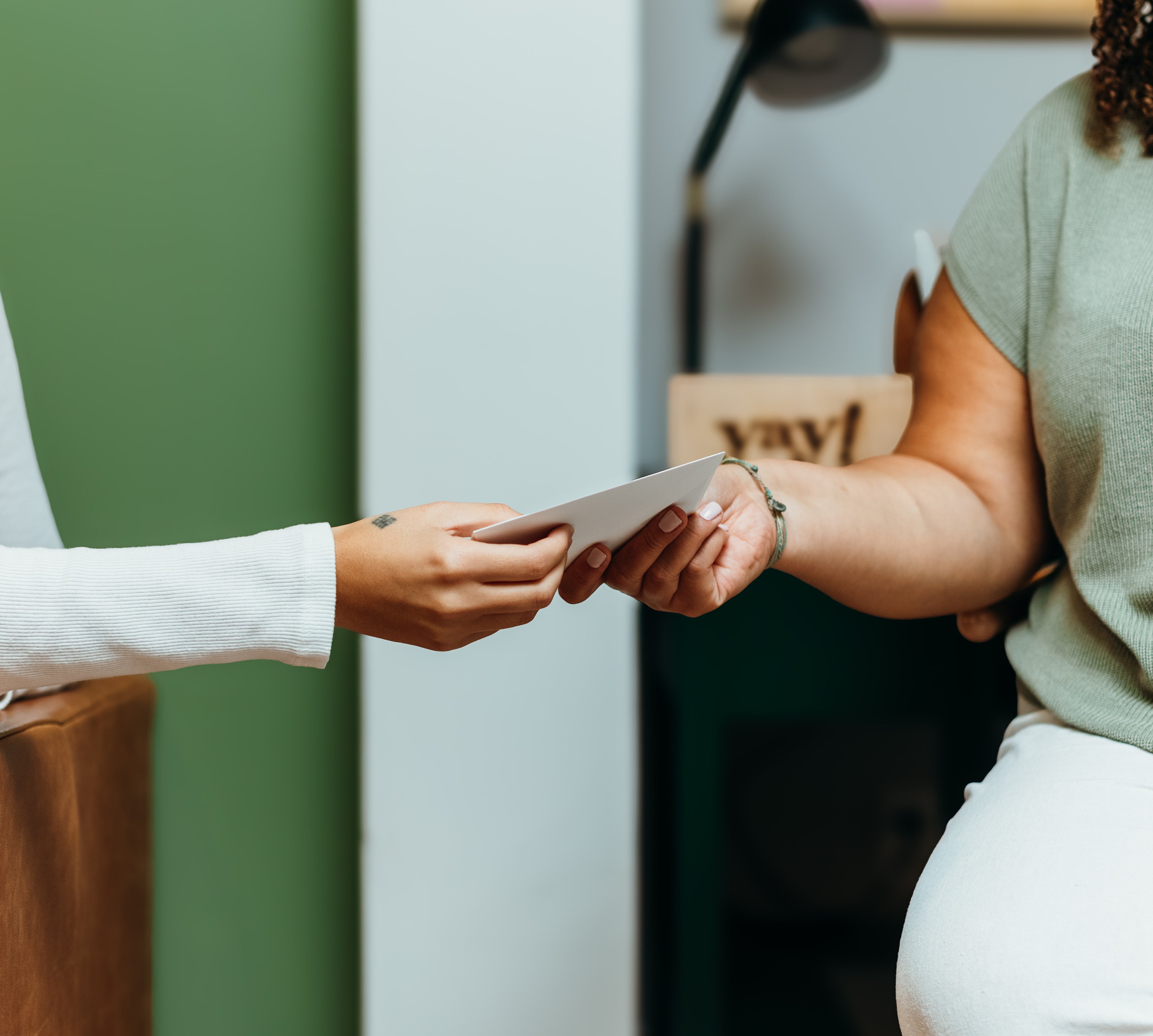 Two people exchanging a card in an indoor setting with a neutral background